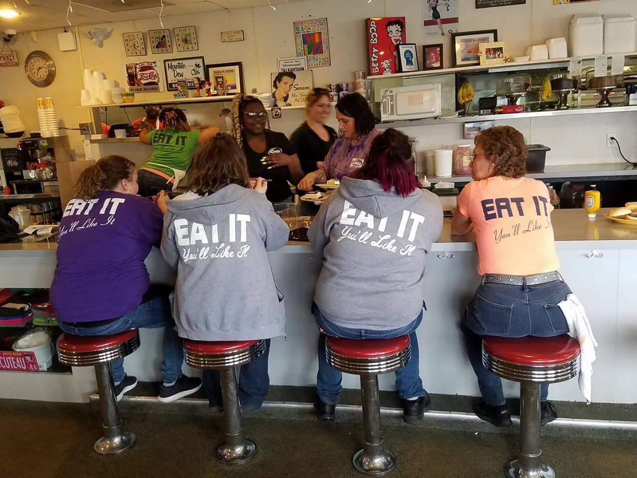 Inside Stella's Diner — the counter, red stools and 'EAT IT' regulars